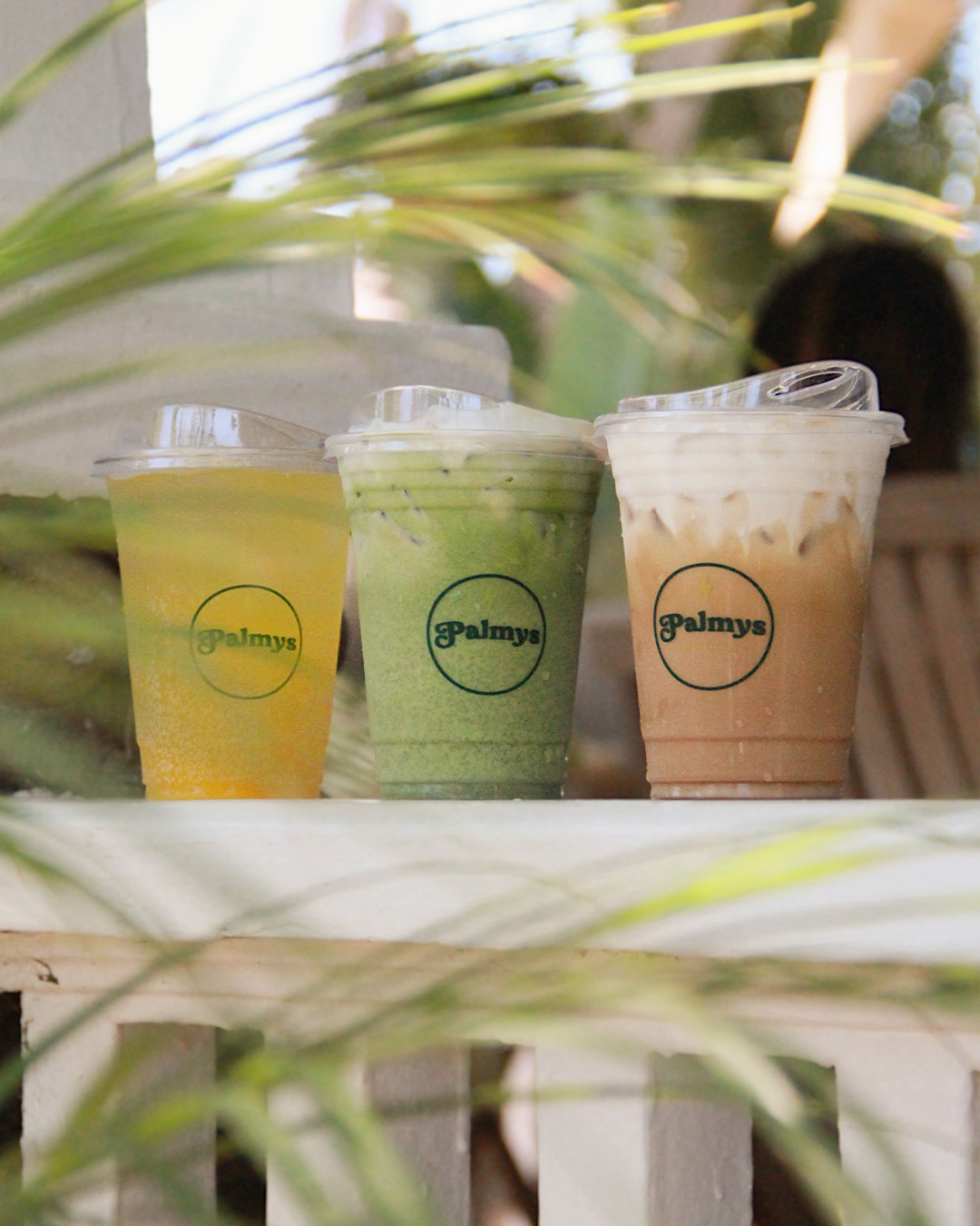 Iced juice, matcha and latte lined up on the patio ledge