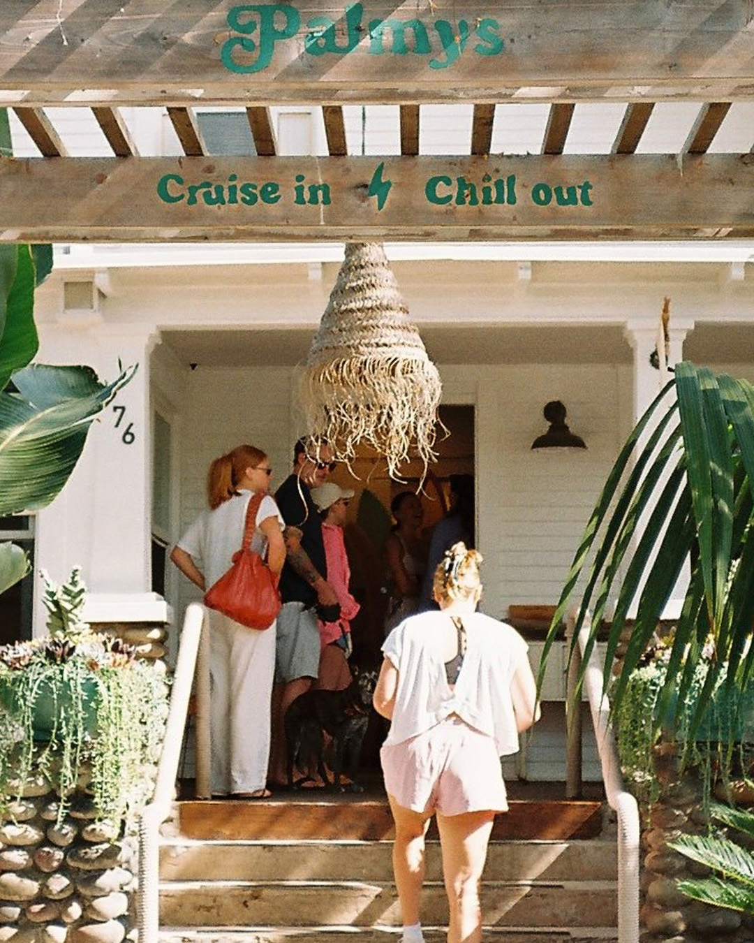 Guests on the Palmys porch beneath the Cruise in, Chill out sign